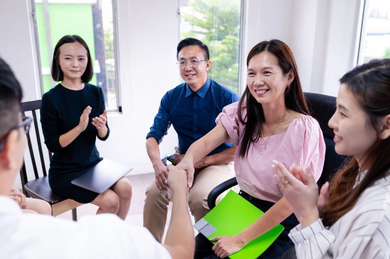 A mid aged businessman shakes hands with his female colleague and praising her contributions during a team-building workshop.