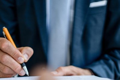 A person in a suit signs a document with a pen. Estate planning services probate wills and trusts