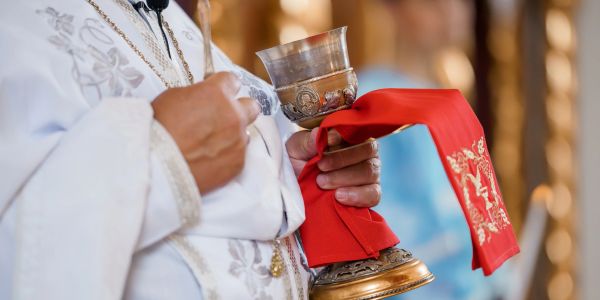 Priest holding a chalice with red cloth during a religious ceremony.
