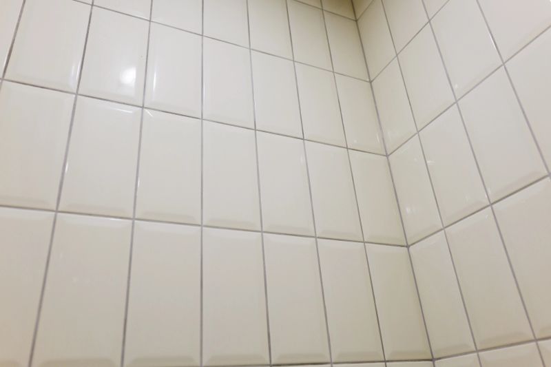 Bright and tidy bathroom corner featuring plain white tiles stacked vertically.