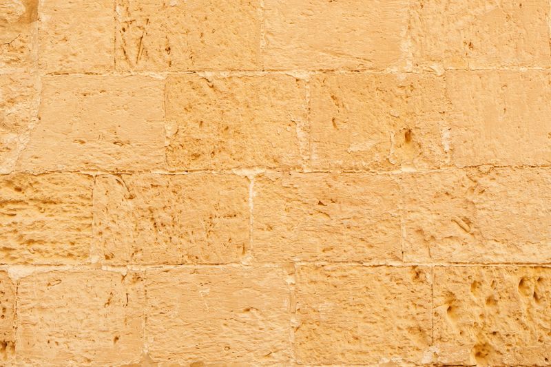 A sunlit beige stone wall with rough, weathered blocks. Evokes warmth, rustic charm, and historic architecture—perfect for editorial features on Malta heritage, travel, or construction aesthetics.
