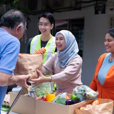 Volunteers handing groceries to an elderly man outdoors.