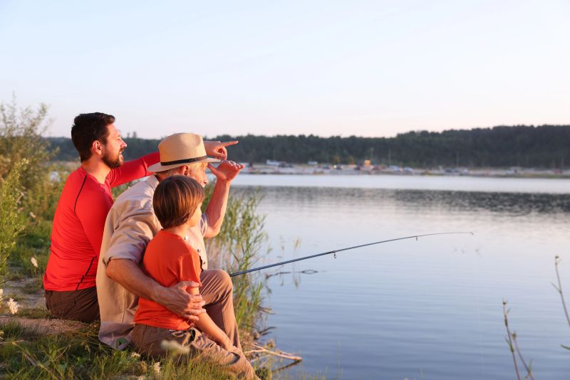 Smiling grandfather, father and his little son fishing together near river outdoors