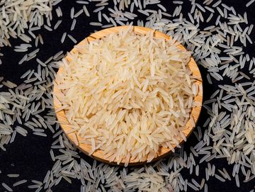A wooden bowl filled with uncooked white rice against a black background.
