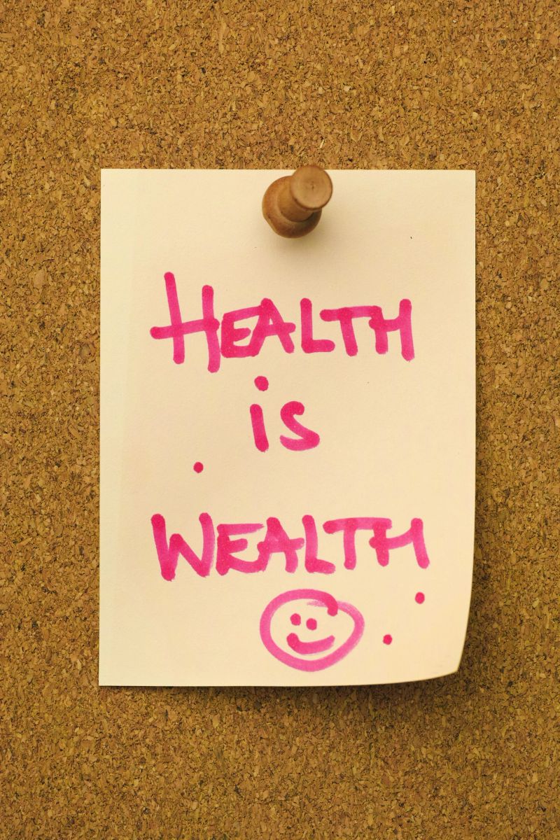 The words 'HEALTH IS WEALTH' written in a pink marker pen on flesh colored note paper, pinned by a wooden pin to a cork message board. Conceptual motivational and inspirational quote message relating to good health, valuable, rich, wealthy, healthy, etc.