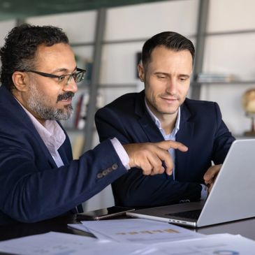 Two professional men discussing work on a laptop in an office.