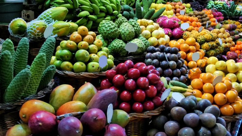 Colorful tropical fruit market display with bananas, dragon fruit, grapes, mangos, kiwis, apples, oranges, exotic fruits in baskets – vibrant fresh produce street food photography