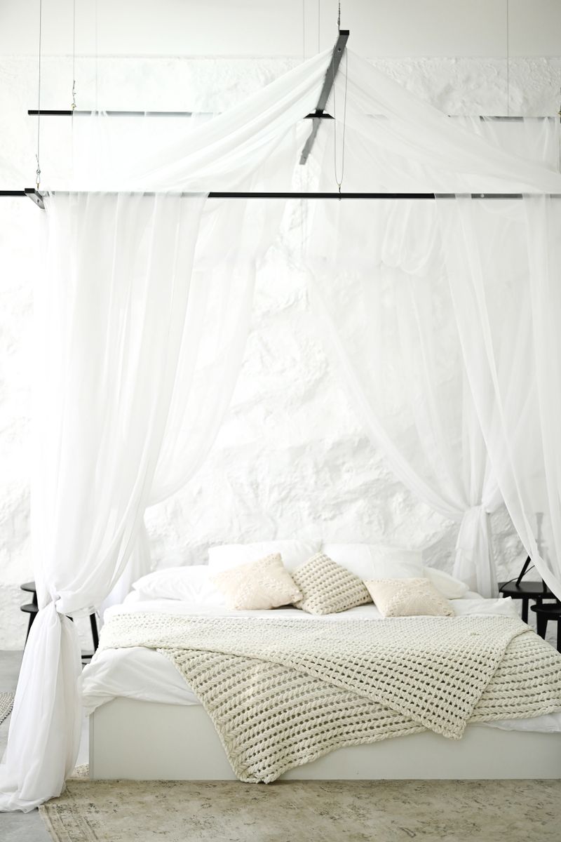 White canopy bed standing in a modern minimalist bedroom with a textured wall