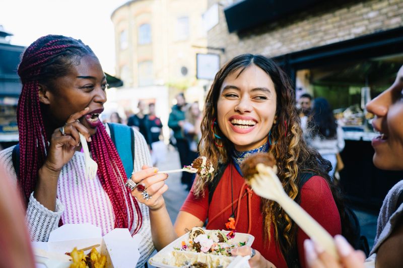 Happy woman in her 30s enjoying street food in market with multi racial female friends, Camden, London