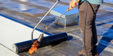 Person applying torch-on waterproofing membrane to flat roof.