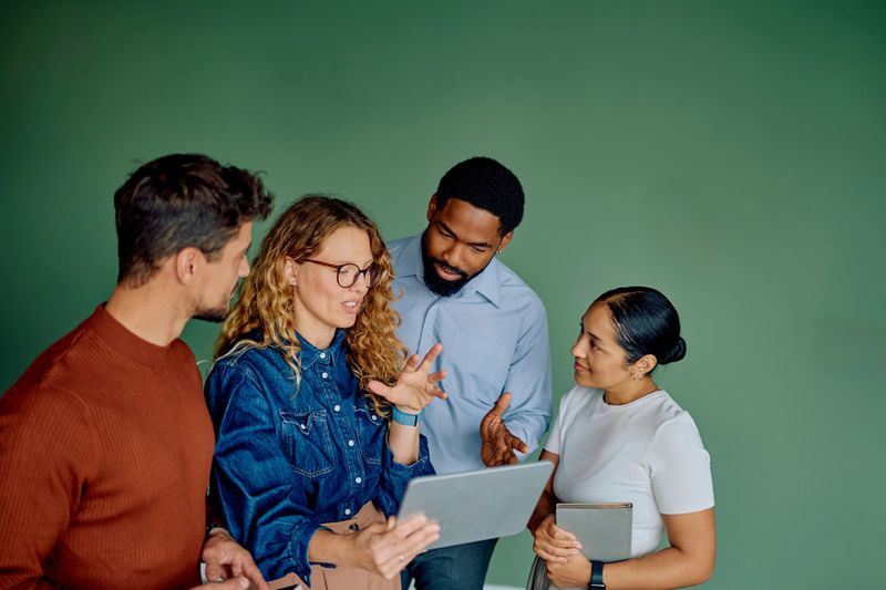 Diverse business team actively discussing ideas and collaborating on a project, using a digital tablet against green background