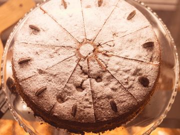 A powdered sugar-topped cake with almond decorations, sliced into pieces.