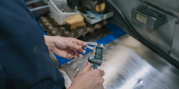 Person measuring an object with a digital caliper in a workshop.