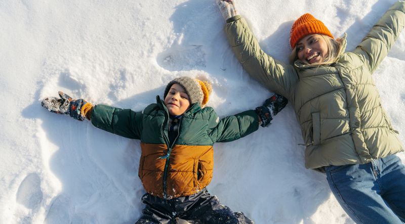 Photo of mother and son making snow angels in the snow