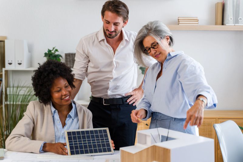 Diverse team of architects discussing a sustainable building model with a miniature solar panel