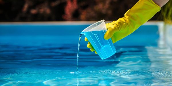 Hand pouring blue liquid into pool water.
