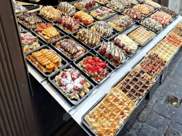 Variety of waffles with fruits and drizzled sauces on display.