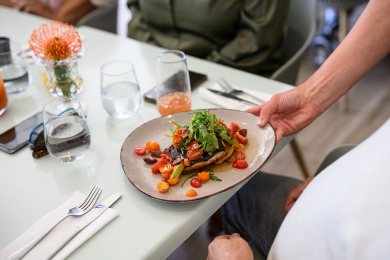 Closeup view of plated vegetable salad with cherry tomatoes and greens being served to guest, reflecting healthy eating, fine dining, and vibrant lifestyle travel.