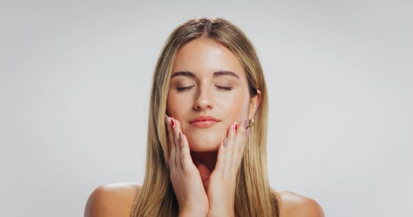 Relaxed woman with eyes closed gently touching her face, showcasing natural beauty.
