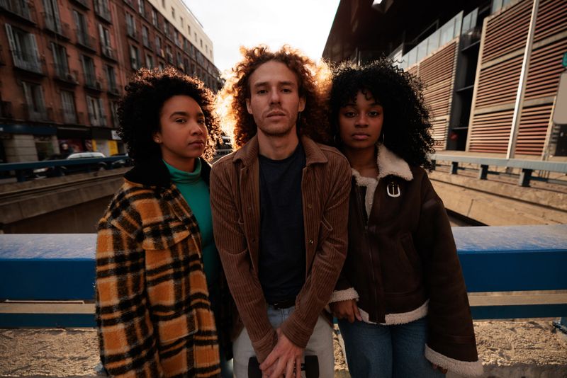 Three young artists standing together in an urban setting, posing confidently as the sun sets behind them