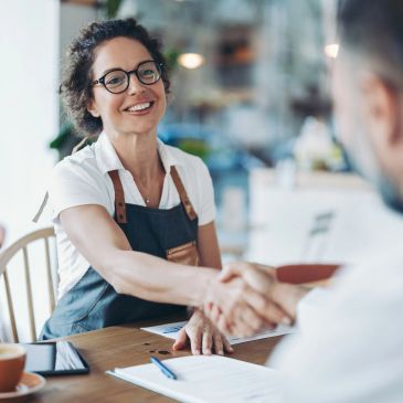 Smiling barista shaking hands with a customer in a cozy cafe.