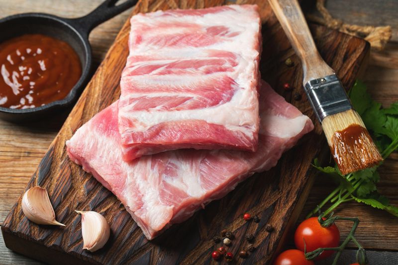 Raw pork ribs with spices, salt and rosemary on dark wooden background.