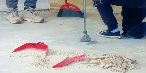 Two people cleaning debris with broom and dustpan on a floor.