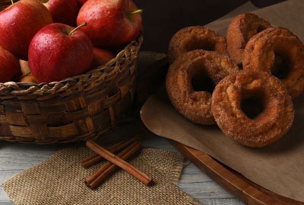 Basket of apples and cinnamon sugar donuts on a wooden table.