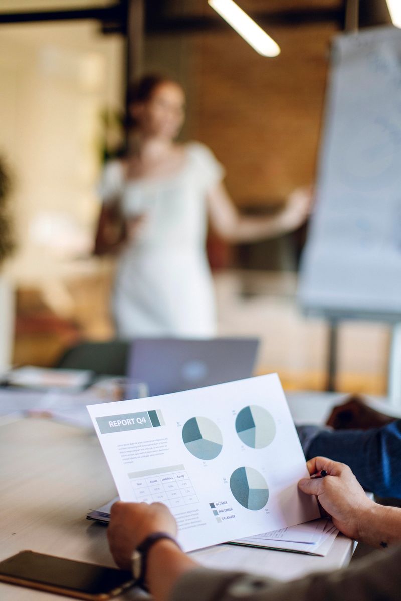 A business meeting where attendees review a quarterly report featuring pie charts and graphs while a presenter discusses key points using a flip chart in a modern office setting