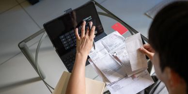 Person managing bills and using a calculator on a tablet at a glass table.