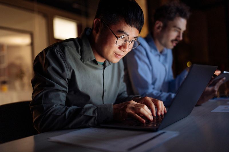 Two colleagues working together in an office setting during night hours, focusing on tasks