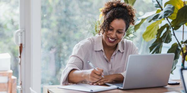 Woman working and writing with a laptop.