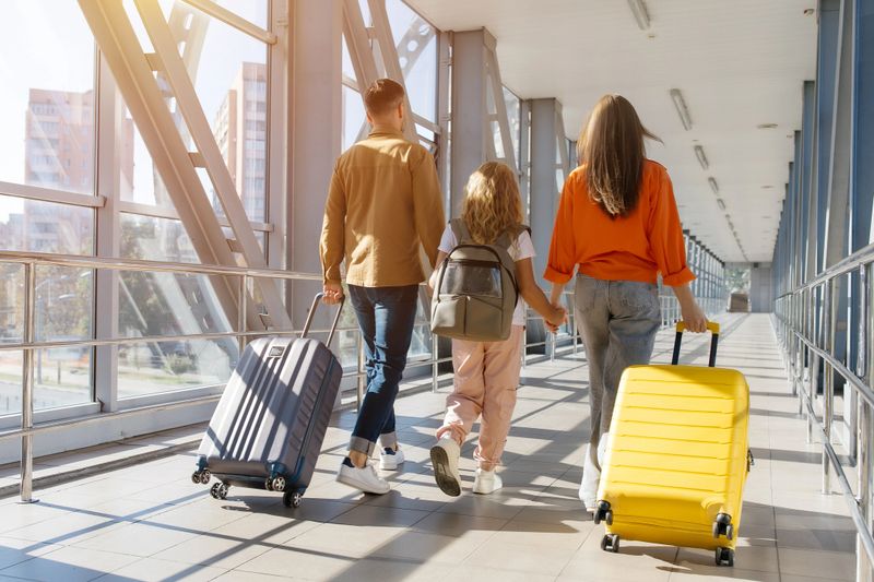 European family walking together at airport corridor with luggage, holding hands and smiling, showing cheerful lifestyle, bonding, unity and joyful holiday departure