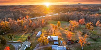 Sunset over a countryside farm with autumn foliage and rustic buildings.