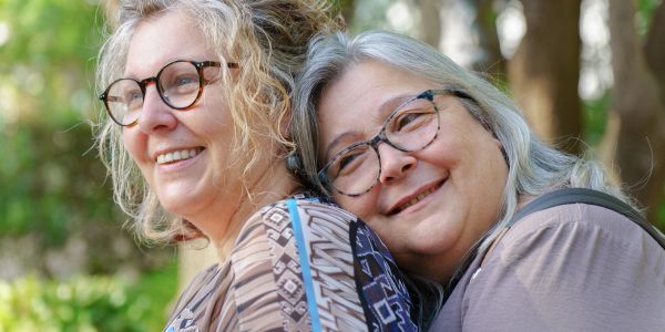 Two smiling older women embracing outdoors.