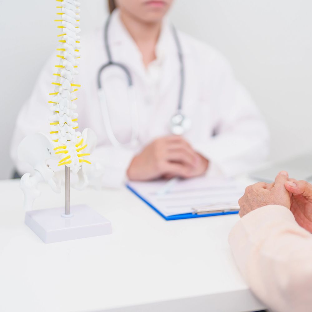 Doctor consulting patient with spine model on desk.