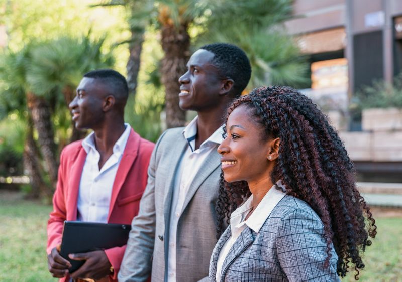 Three elegant multiracial business people looking up and smiling outdoors, teamwork concept