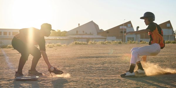Two kids playing baseball at sunset.