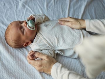 Newborn baby peacefully sleeping with a pacifier, held gently by caring hands.