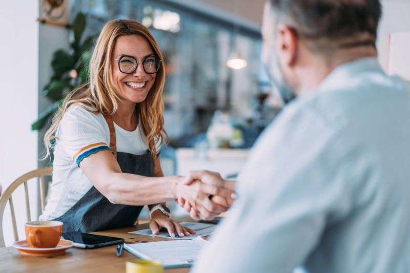 Shot of female cafe owner shaking hands with a financial consultant during a business meeting. Concept of small business financing, loans, entrepreneurship, investment, and support for local businesses.