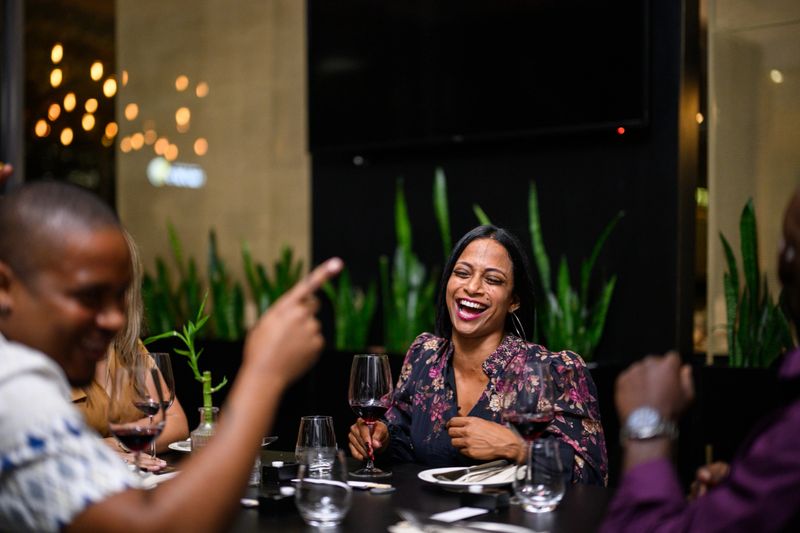 Friends enjoying conversation and drinks at a restaurant table, with warm golden lighting, decorative plants and a relaxed social atmosphere enhancing the evening.