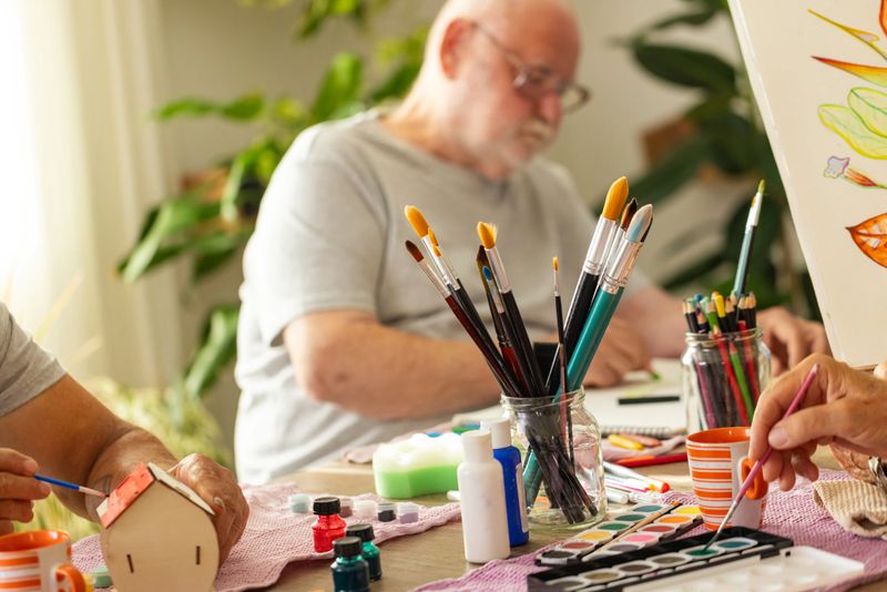A detailed close-up shot of paint brushes and art supplies, with happily engaged man painting in the background.