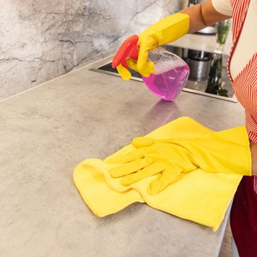 Person cleaning a kitchen countertop with gloves and spray bottle.