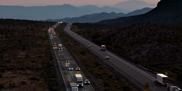Highway traffic at dusk with mountains silhouetted against the colorful sky.