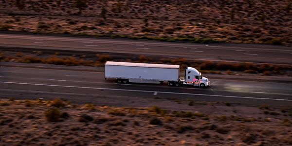A white semi-truck drives on a desert highway at dusk.