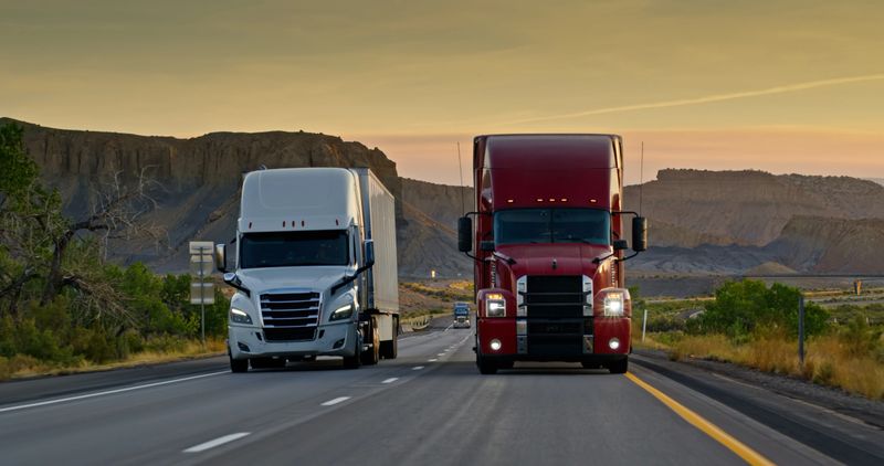 Vehicle mounted shot looking back at two trucks driving on Interstate 70 in Emery County, Utah at sunset.