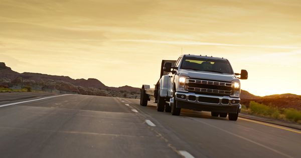 Silver truck driving on an open highway at sunset.