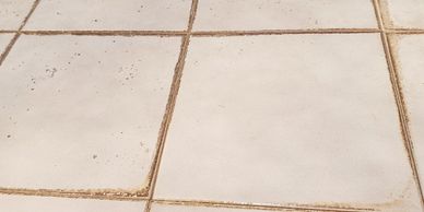 Dirty white floor tiles with brown grime in the grout lines.