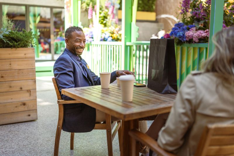 A cheerful business meeting taking place outdoors with two professionals enjoying coffee and conversation in a vibrant setting. 5th Ave, Manhattan, NYC