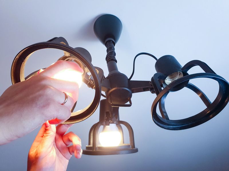A woman screws an LED light bulb into a chandelier by hand, replacing a lamp, home lighting.